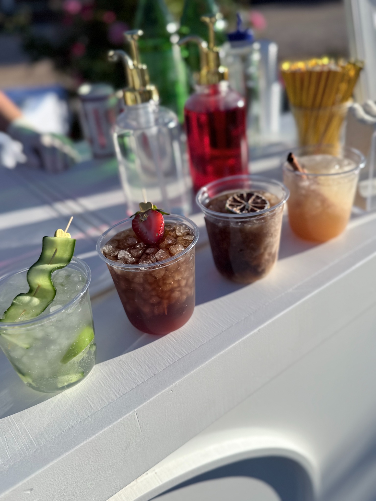 Four garnished drinks on the white Golden Hour Events bar, with syrup bottles and gold straws behind them