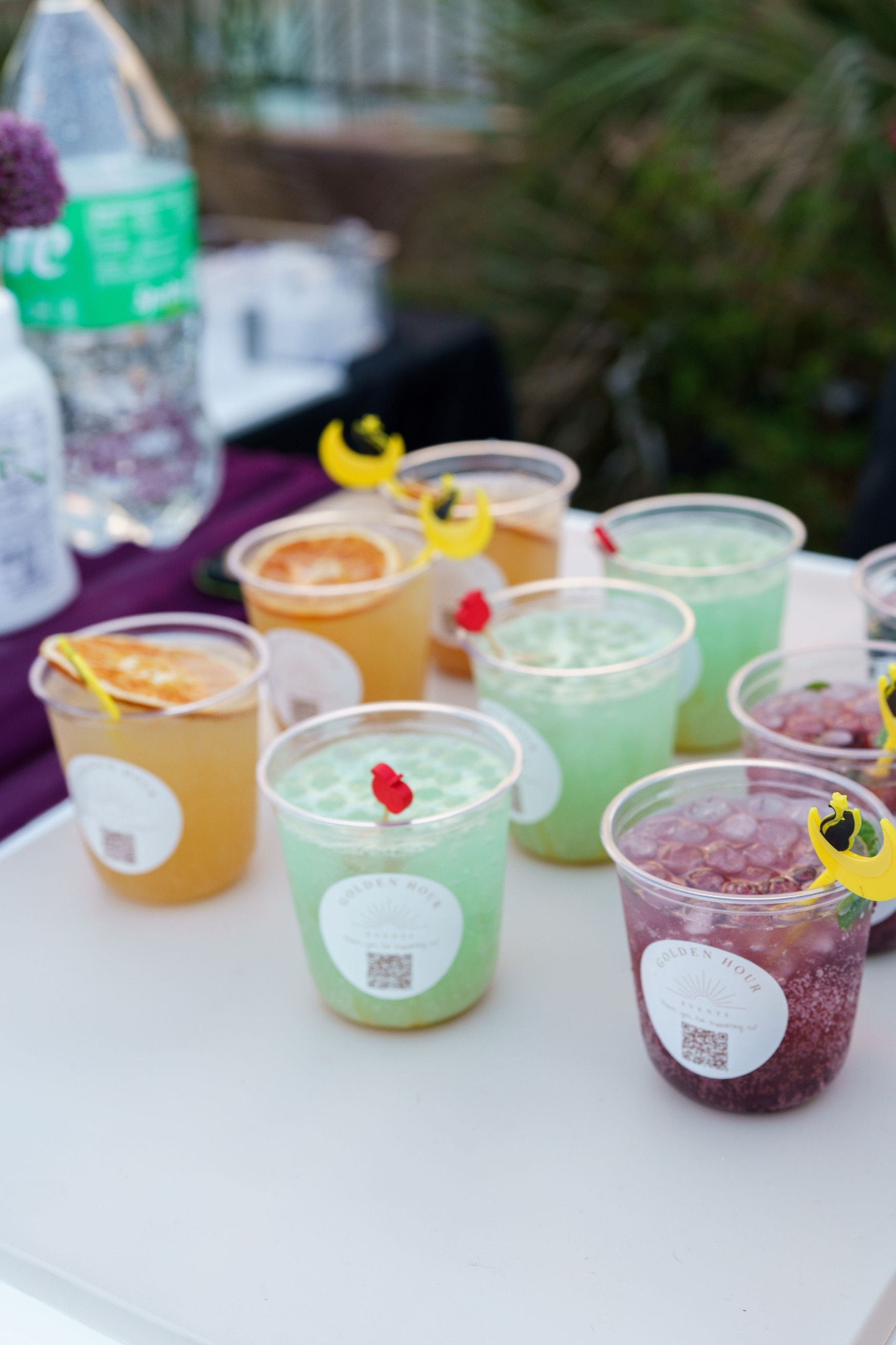 Orange, green and purple iced drinks in Golden Hour Events cups with dried citrus and Halloween stirrers