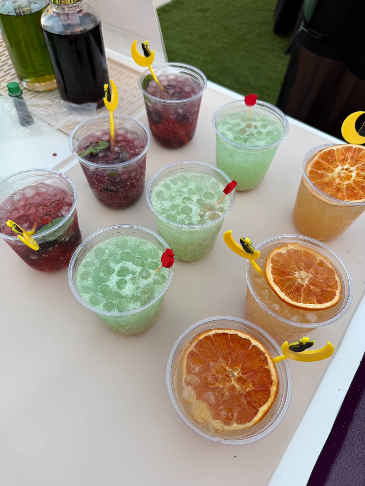 An angled overhead view of purple, green and orange iced drinks with berries, mint, dried citrus and Halloween picks